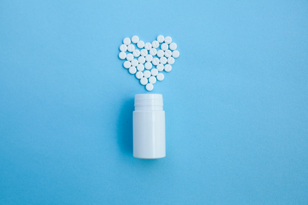 medicine, healthcare and pharmacy concept - pills and of drugs in shape of the heart white tablets are laid out in the shape of a heart and white plastic jar on a blue background with copy spaceの写真素材