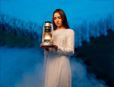 Mysterious mystical girl in a dark night forest with a kerosene lamp in her hands Halloween concept