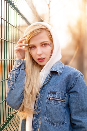 Young Woman with temporary painted flowers on the face. teenage girl with long blond hair wear jeans jacket and hoody .の写真素材