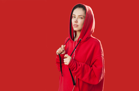 Beautiful caucasian sporty woman to trendy red hoodie on corall color background in studioの写真素材