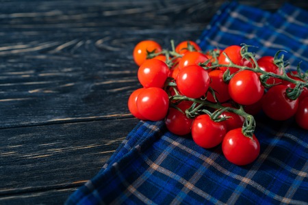 Cherry tomatoes in the checkered cloth serviette on the dark wooden table. Juicy ripe vegetables on a black background. Healthy eating. vegetarian foodの写真素材