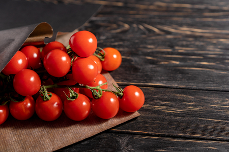 Cherry tomatoes in the paper packaging on the dark wooden table. Juicy ripe vegetables on a black background. Healthy eating. vegetarian foodの写真素材
