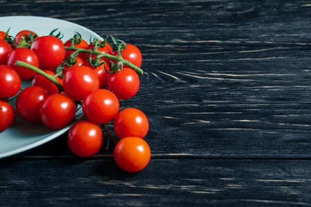 Cherry tomatoes in the white plate on the dark wooden table. Juicy ripe vegetables on a black background. Healthy eating. vegetarian foodの写真素材