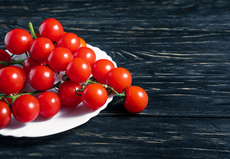 Cherry tomatoes in the white plate on the dark wooden table. Juicy ripe vegetables on a black background. Healthy eating. vegetarian foodの写真素材