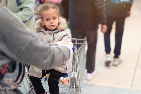 Little girl sitting in a supermarket trolley Young buyer conceptの写真素材