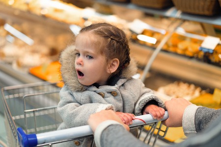 Little girl opened her mouth in surprise while sitting in a supermarket trolley Young buyer conceptの写真素材