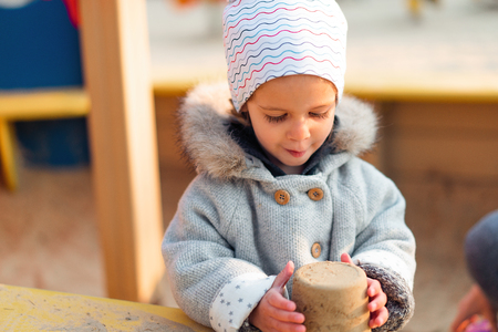 Autumn. Little girl making sand figures in a children sandbox. Children fashion coatの写真素材