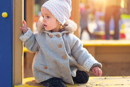 little cute girl playing at the playground in autumn Dressed in the gray fashionable coatの写真素材