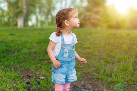 Summer season. Little Caucasian girl walks on nature dressed in denim overalls. Children's fashion. childhoodの写真素材