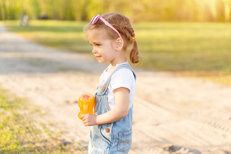 Summer season. Little Caucasian girl walks on nature dressed in denim overalls. Children's fashion. childhoodの写真素材