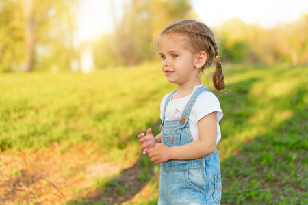 Summer season. Little Caucasian girl walks on nature dressed in denim overalls. Children's fashion. childhoodの写真素材