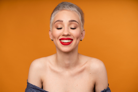 Portrait of young girl with blond short hairstyle looking at camera and laugh isolated on orange background with copy space. Woman surprised and smiling. positive emotionの写真素材