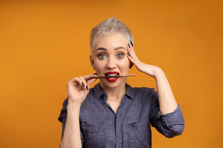 Close up portrait makeup artist. Make up courses. Concept of self visage masterclasses. Fashion professional. Woman hold makeup brushes on the hands. Studio shot on the orange color backgroundの写真素材