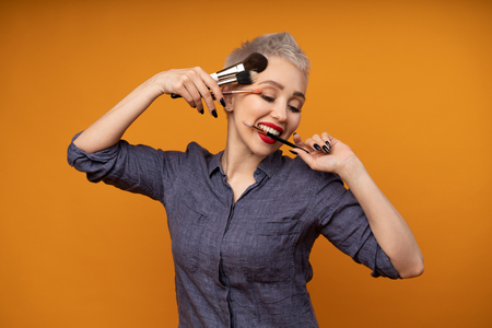 Close up portrait makeup artist. Make up courses. Concept of self visage masterclasses. Fashion professional. Woman hold makeup brushes on the hands. Studio shot on the orange color backgroundの写真素材