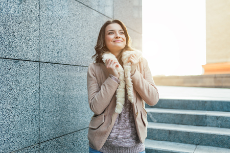 A beautiful young brunette girl walks through the autumn city in the rays of warm sunlight. Enjoys warm weather.の写真素材