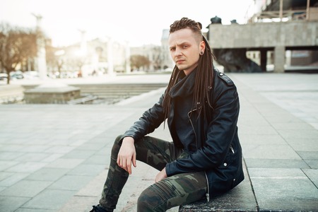 rocker rock star young caucasian man with dreadlocks walking on the city street autumn day. Dressed in the leather jackedの写真素材
