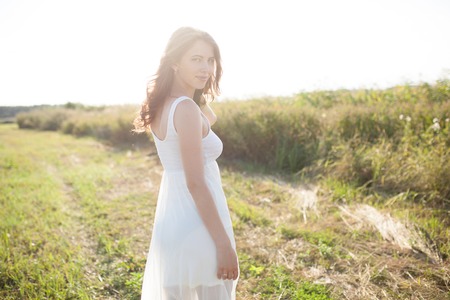 Portrait of woman on the summer field on light background. Pretty young girl. Sunny summer day. Green grass field. Summer background. Outdoor portrait, day light. Rural landscape.の写真素材