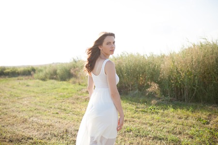 Portrait of woman on the summer field on light background. Pretty young girl. Sunny summer day. Green grass field. Summer background. Outdoor portrait, day light. Rural landscape.の写真素材