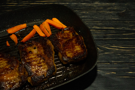 Juicy piece of fried meat in a pan that stands on a black wooden table background with copy spaceの写真素材