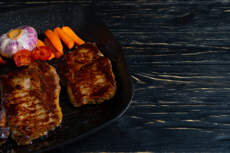 Juicy piece of fried meat in a pan that stands on a black wooden table background with copy spaceの写真素材