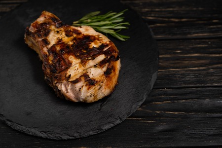 A juicy piece of fried meat lies on a stone plate against a black wooden table. Degree of roasting well done. Food concept with copy spaceの写真素材