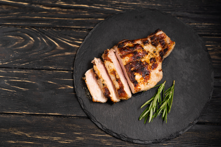 A juicy piece of fried meat lies on a stone plate against a black wooden table. Degree of roasting well done. Food concept with copy spaceの写真素材