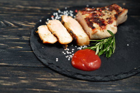 A juicy piece of fried meat lies on a stone plate against a black wooden table. Degree of roasting well done. Food concept with copy spaceの写真素材