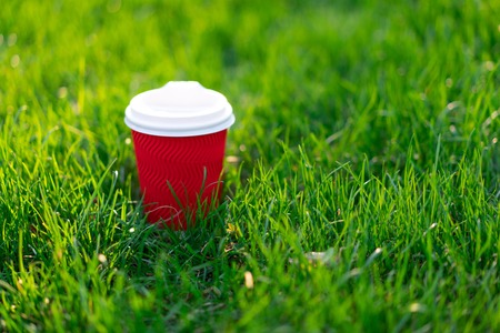 A red disposable cardboard cup with hot tea stands in fresh green grass. morning fresh conceptの写真素材