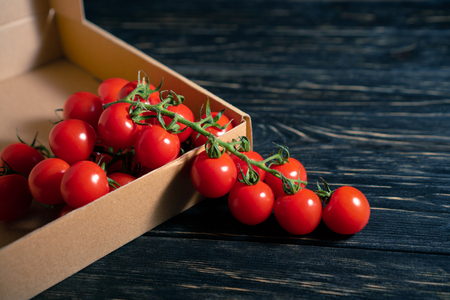 Cherry tomatoes in the cardboard box on the dark wooden table. Juicy ripe vegetables on a black background. Healthy eating. vegetarian foodの写真素材