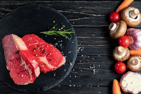 On one side of the table are vegetables on the other side of a beautiful juicy, raw beef meat. Choose your food. Healthy eating conceptの写真素材