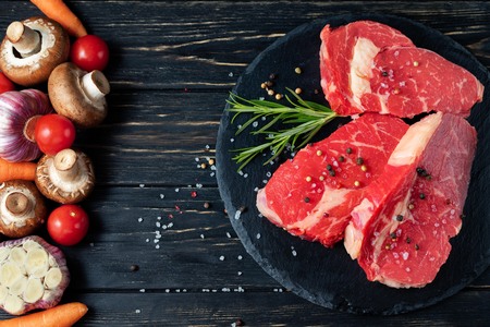 On one side of the table are vegetables on the other side of a beautiful juicy, raw beef meat. Choose your food. Healthy eating conceptの写真素材
