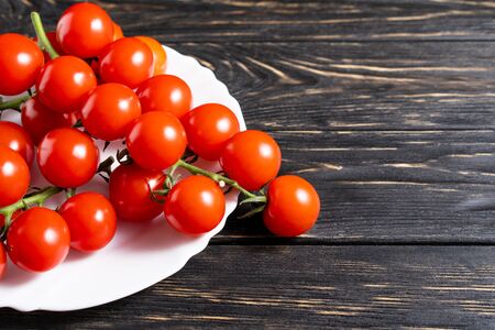 Cherry tomatoes in the white plate on the dark wooden table. Juicy ripe vegetables on a black background. Healthy eating. vegetarian foodの写真素材