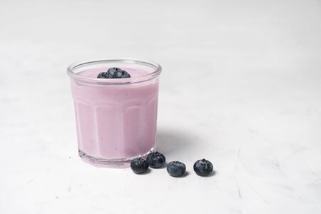 Tasty fresh blueberry yoghurt shake dessert in glass standing on white table background. Homemade berry smoothie. Healthy eating. Diet food yogurtの写真素材