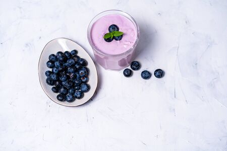 Tasty fresh blueberry yoghurt shake dessert in glass standing on white table background. Homemade berry smoothie. Healthy eating. Diet food yogurtの写真素材