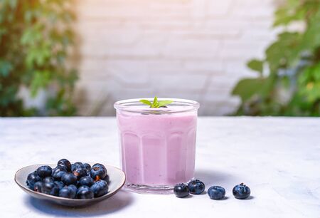 Tasty fresh blueberry yoghurt shake dessert in glass standing on white table background. Homemade berry smoothie. Healthy eating. Diet food yogurtの写真素材