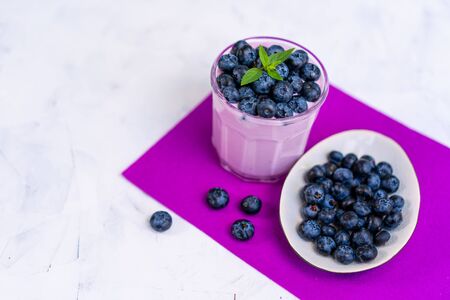 Tasty fresh blueberry yoghurt shake dessert in glass standing on white table purple napkin background. Homemade berry smoothie. Healthy eating. Diet food yogurtの写真素材