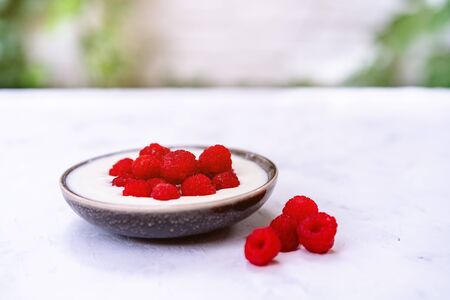 Tasty fresh raspberries yoghurt shake dessert in ceramic bowl standing on white table background....