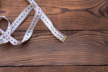 White measuring tape of a tailor lies in corner on dark wooden background. Copy space for text