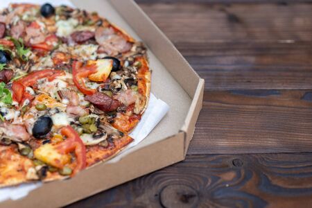 Appetizing pizza with smoked sausages bacon meat tomato cheese arugula cardboard boxes for delivery on black dark background. With copy space for textの写真素材