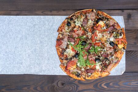 Appetizing pizza with smoked sausages bacon meat tomato cheese arugula cardboard boxes for delivery on black dark background. With copy space for textの写真素材