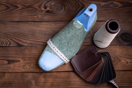 Leather samples for shoes and plastic shoe last on dark wooden table. Designer furniture clothes....