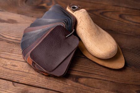 Leather samples for shoes and wooden shoe last on dark wooden table. Designer furniture clothes....