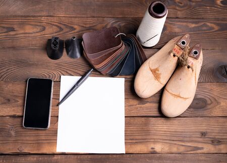 Leather samples for shoes and wooden shoe last on dark wooden table with Empty white sheet of paper...