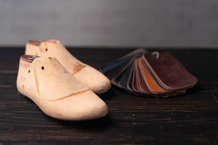 Leather samples for shoes and wooden shoe last on dark wooden table. Designer furniture clothes....