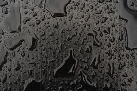 Rain water drops on black surface. Liquid on dark wooden background. Abstract concept with dark mood.の写真素材