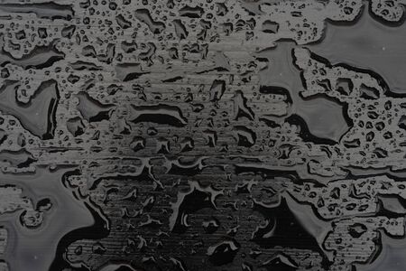 Rain water drops on black surface. Liquid on dark wooden background. Abstract concept with dark mood.の写真素材