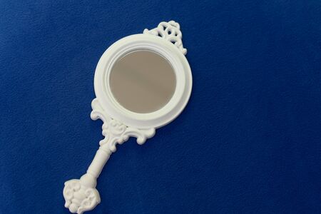 Vintage style white women hand mirror with decoration, women gadget, beauty concept with free space lies on dark blue towel.の写真素材