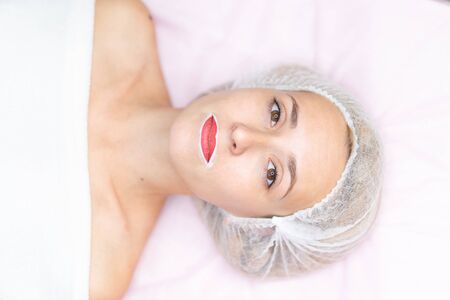 Cosmetology cabinet client lies on couch. Beautician applies marking on lips. Preparation for the procedure of permanent lips makeup. Close up. Beauty industryの写真素材