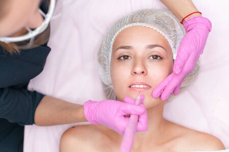 Cosmetology cabinet client lies on couch. Beautician applies marking on lips. Preparation for the procedure of permanent lips makeup. Close up. Beauty industryの写真素材