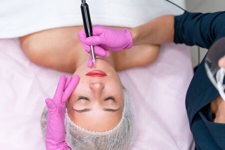 Cosmetology cabinet client lies on couch. Beautician applies marking on lips. Preparation for the procedure of permanent lips makeup. Close up. Beauty industryの写真素材